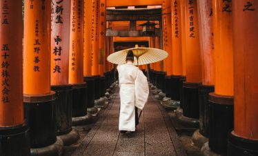 A person in traditional attire walks through the iconic torii gates at Fushimi Inari Shrine, Kyoto.