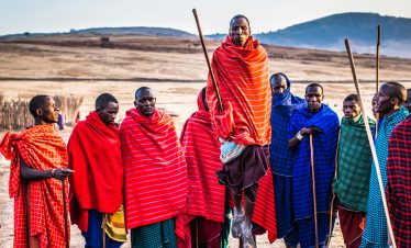 A group of Maasai men in vibrant traditional attire performing a cultural jumping dance outdoors.