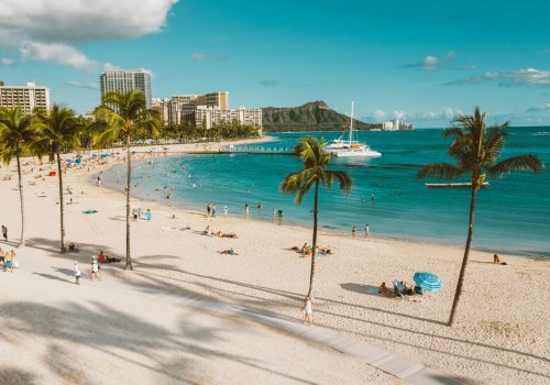 Sunny day at Waikiki Beach with a view of Diamond Head and people enjoying the ocean.