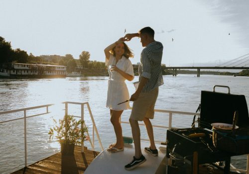 A couple enjoys a romantic dance on a yacht during a vibrant sunset with scenic river views.